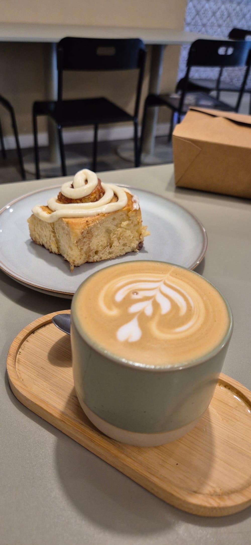 Rollo de canela y latte con arte sobre una bandeja de madera en ZĒSTE