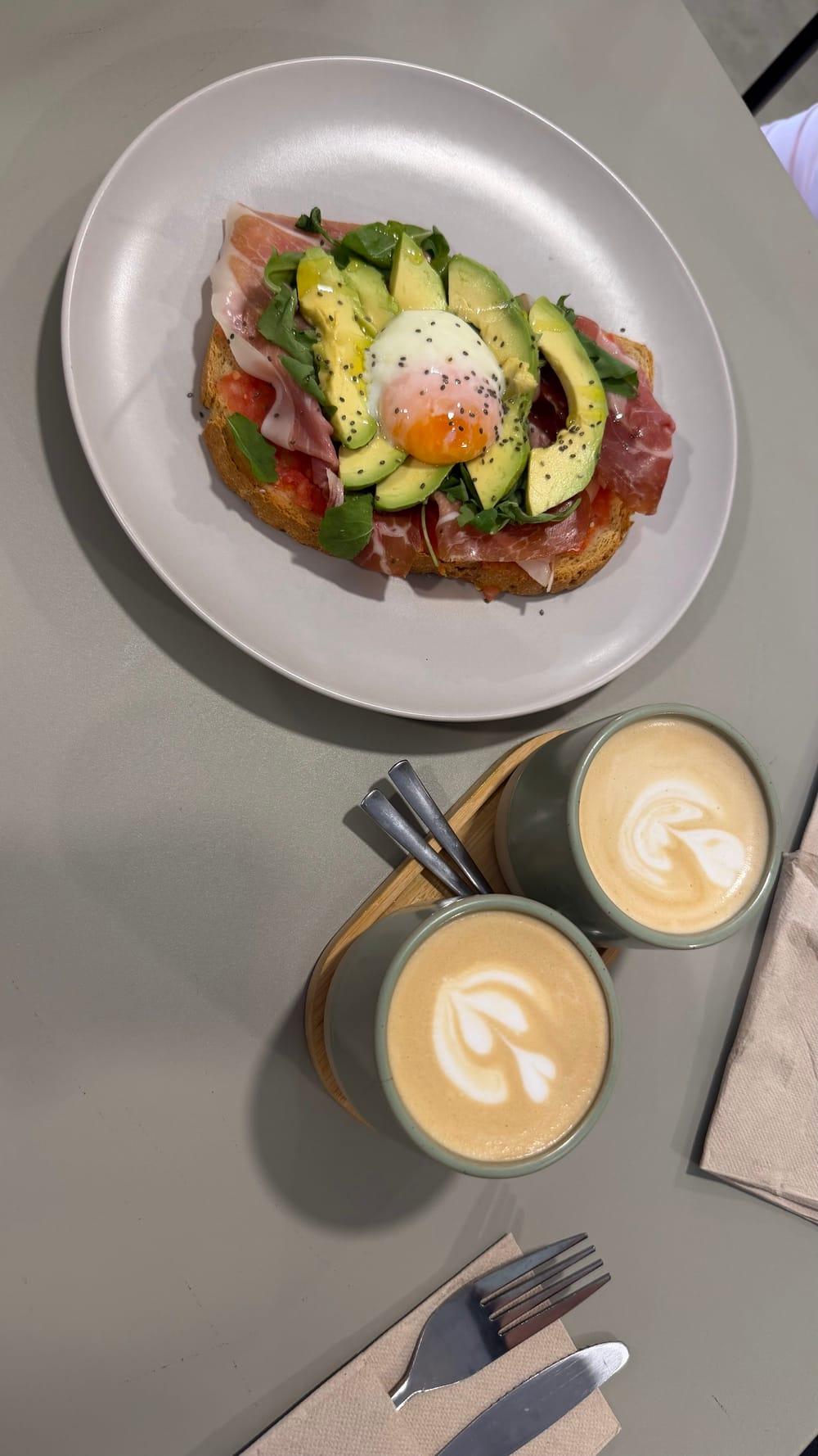 Tostada de aguacate y dos lattes en una mesa de ZĒSTE